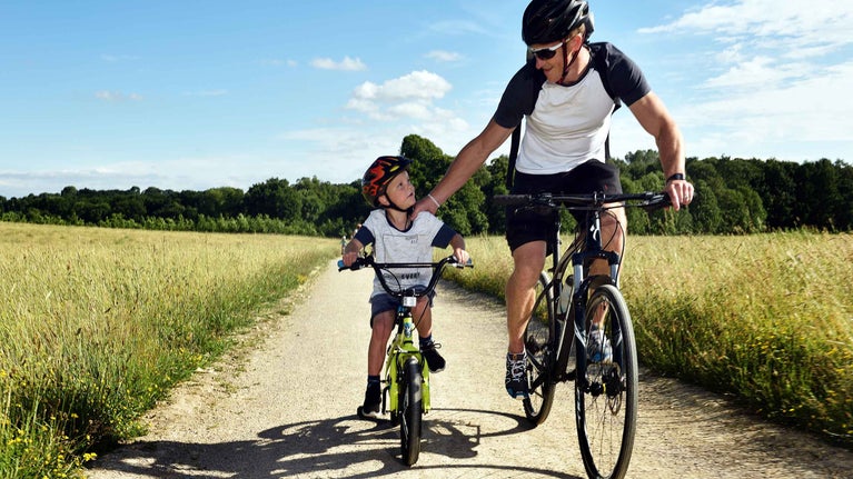 An adult and a young boy riding their bikes on a path at Nostell Priory